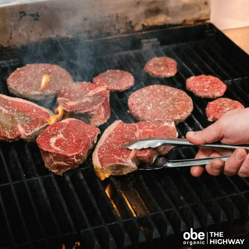 Cuts of steak and burger patties grilling over open flame.