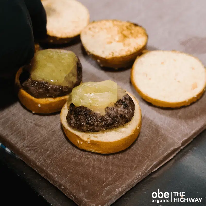 Burger patties with melted cheese next to sliced buns on a counter.