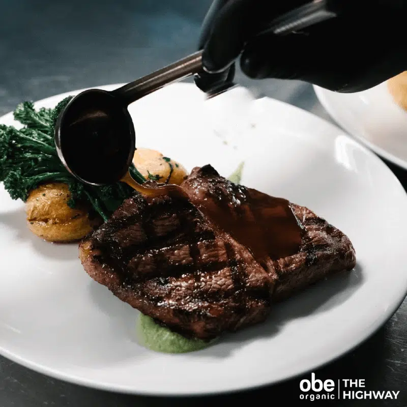 Seared steak served with greens and red wine sauce being poured.