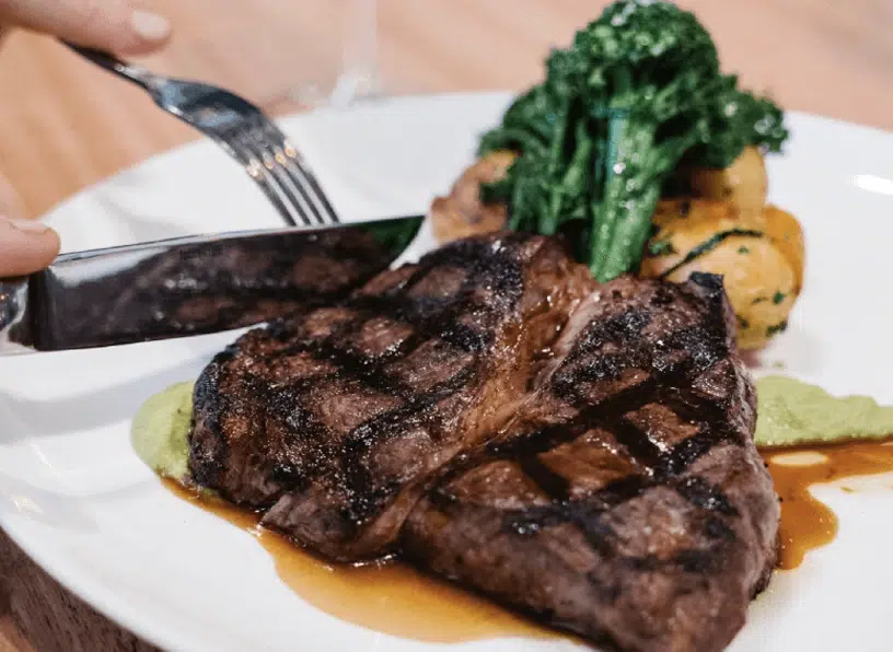 Grilled steak served with vegetables and sauce on a white plate.