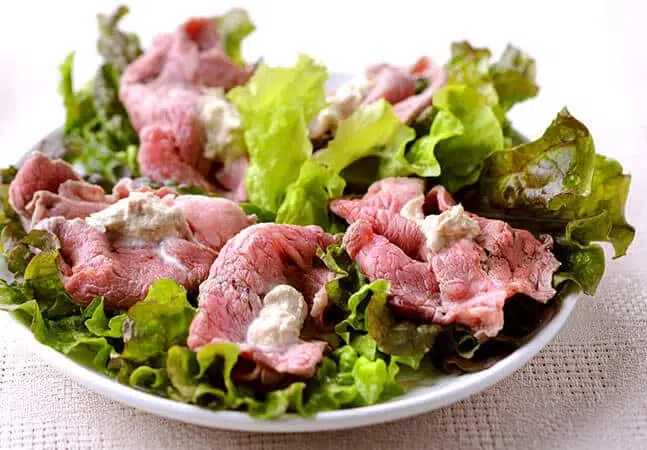 Plate of roast beef slices served on fresh lettuce leaves with a creamy sauce topping.