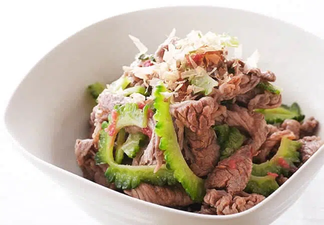 Bowl of stir-fried beef with sliced bitter melon, topped with bonito flakes.