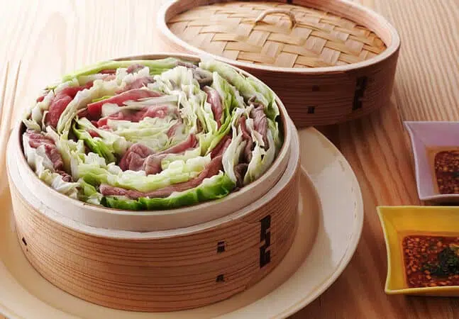 Steamed dish of layered beef and cabbage arranged in a spiral inside a bamboo steamer basket.