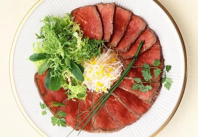 Plate of thinly sliced roast beef arranged in a circle with mixed greens, shredded vegetables, and fresh herbs in the center.